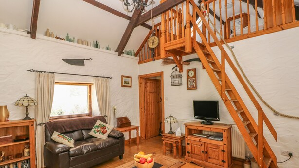 A cozy living room with a wooden staircase, a leather sofa, a wooden coffee table, and a television. - Bluebell Cottage (Milford Haven)
