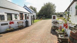 A quaint village street with a white building labeled "CHURCH VIEW" on the left, a wooden bench, and a cart with flowers. - Bluebell Cottage (Milford Haven)