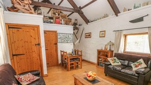 A cozy living room with wooden furniture, a dining table, and a leather sofa. - Bluebell Cottage (Milford Haven)