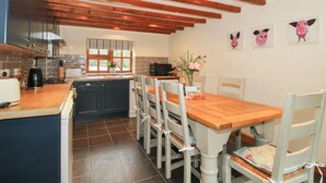 Une cuisine avec des poutres en bois, une table à manger avec des chaises et une fenêtre donnant sur un paysage verdoyant.