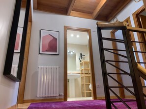 Un escalier menant à une salle de bain équipée d’un radiateur blanc, d’un tableau encadré au mur et d’un tapis violet.