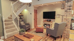 A living room with a staircase, a television, and a fireplace. - The Olde Stables (Morpeth)