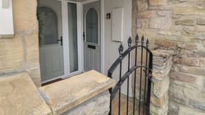 A stone facade with a white door and a black metal gate. - The Olde Stables (Morpeth)