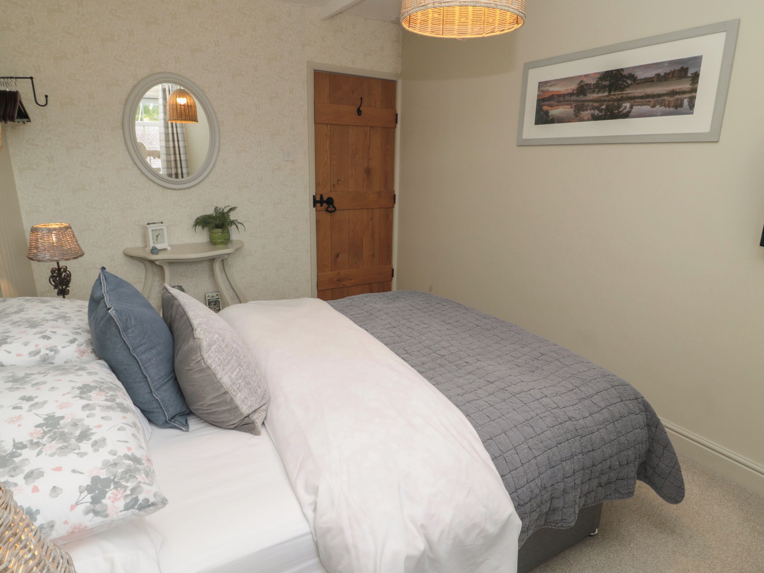 A bedroom with a bed, a bedside table with a lamp, a mirror, a door, and a framed picture on the wall.