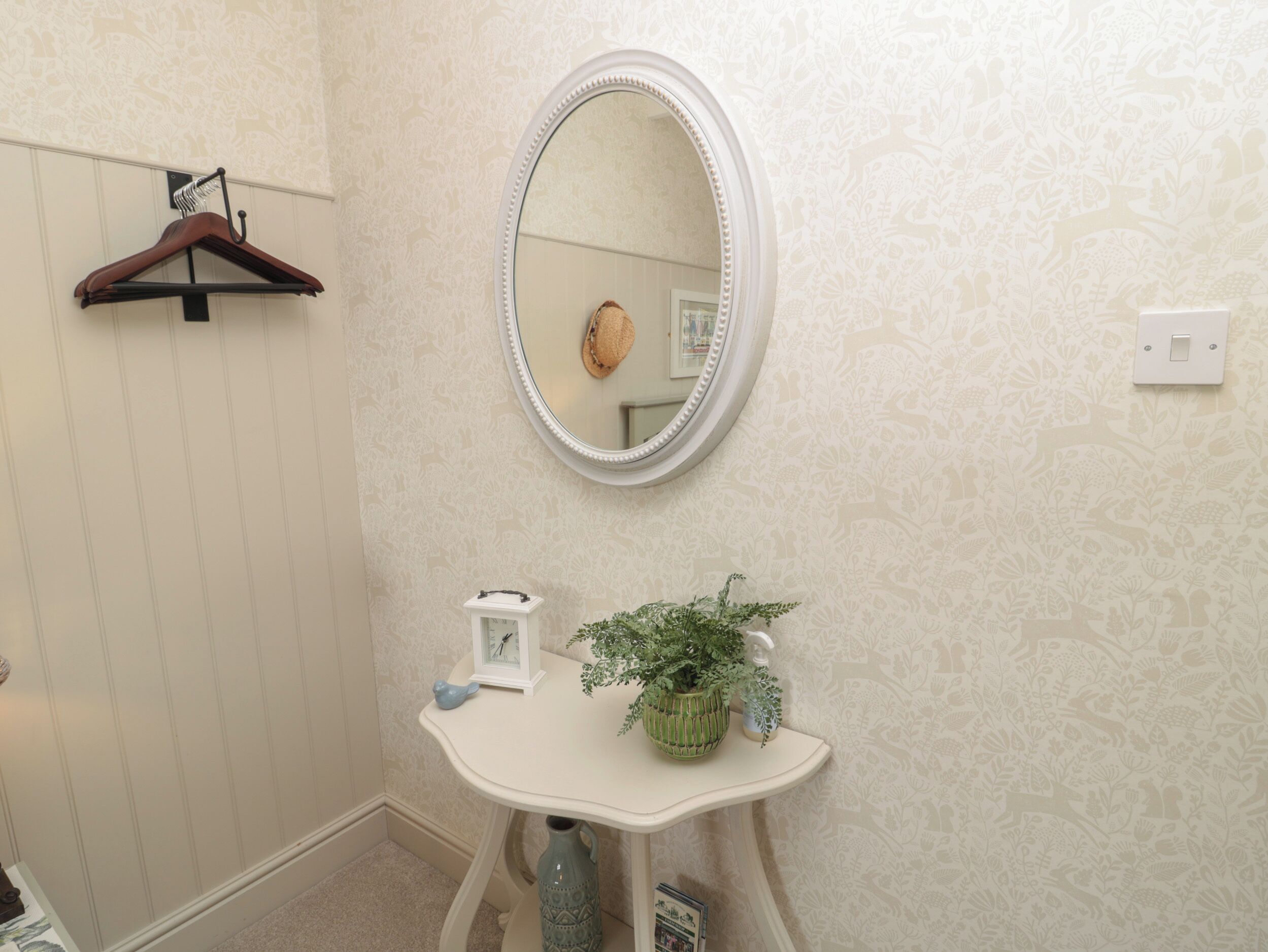 A bathroom with a white vanity, a round mirror, a hanging coat rack, and a potted plant.