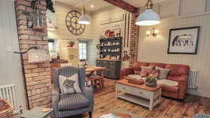 A cozy living room with a brick wall, a striped armchair, a brown leather sofa, and a wooden coffee table. - The Olde Stables (Morpeth)