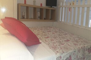 A bedroom with a bed, a wooden shelf, and a television.