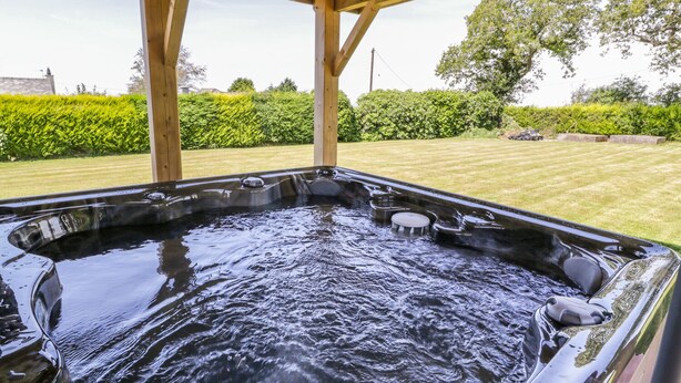 Un bain à remous sous une pergola en bois, avec une pelouse verdoyante et des haies en arrière-plan.