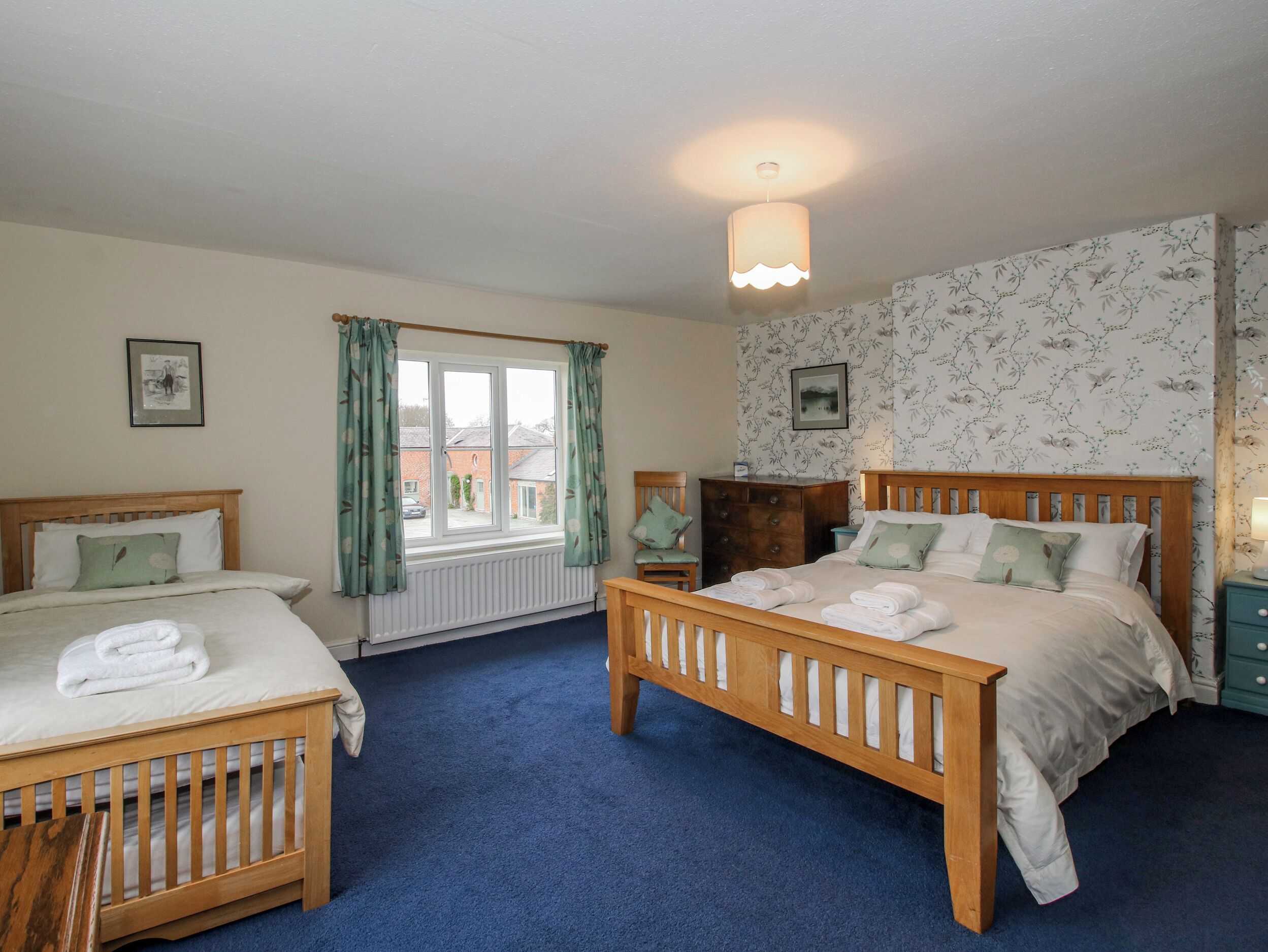 A bedroom with two beds, a dresser, a chair, a radiator, and a window with curtains.