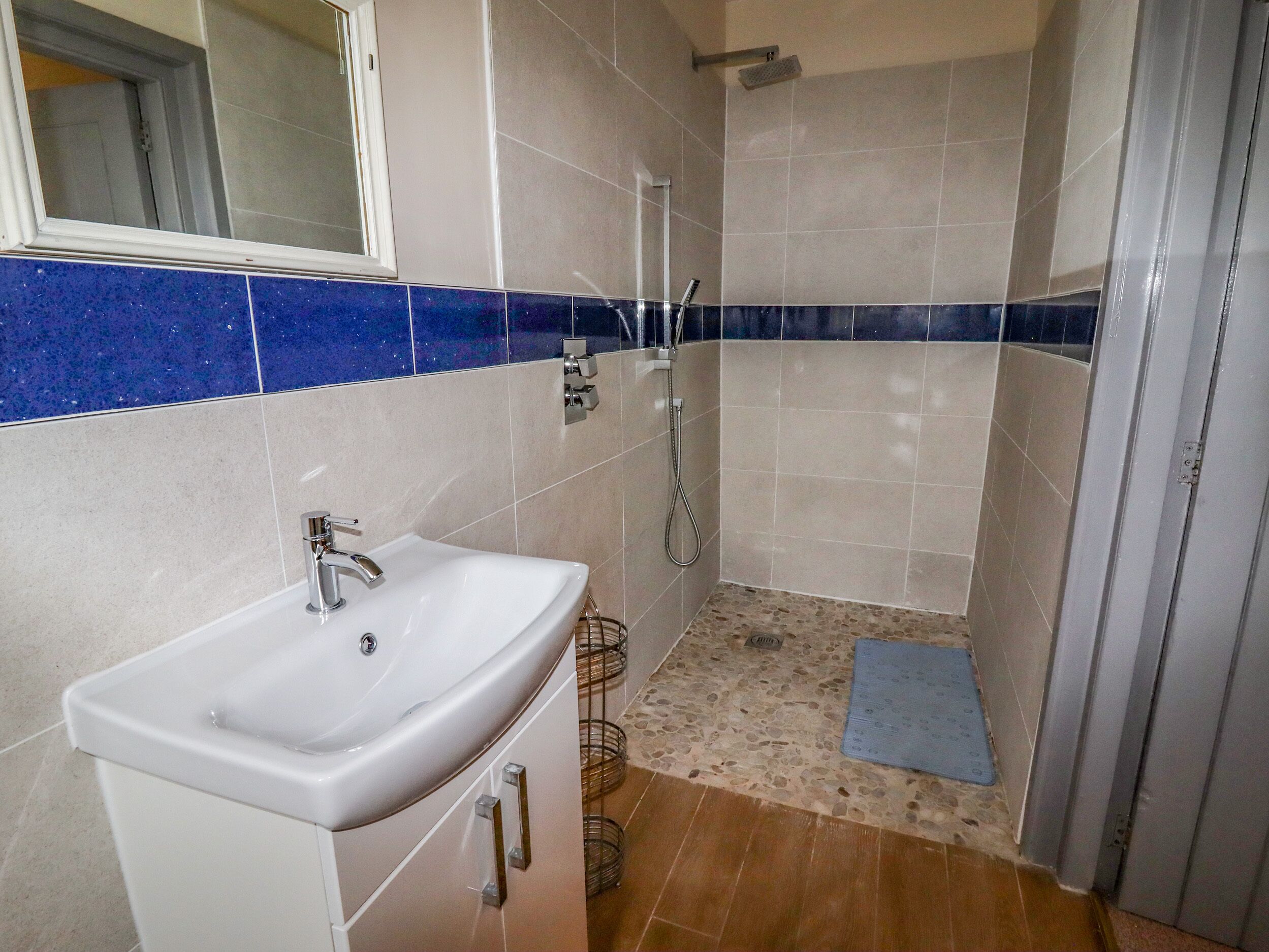 A bathroom with a white sink, a shower, and a blue-tiled shower area.