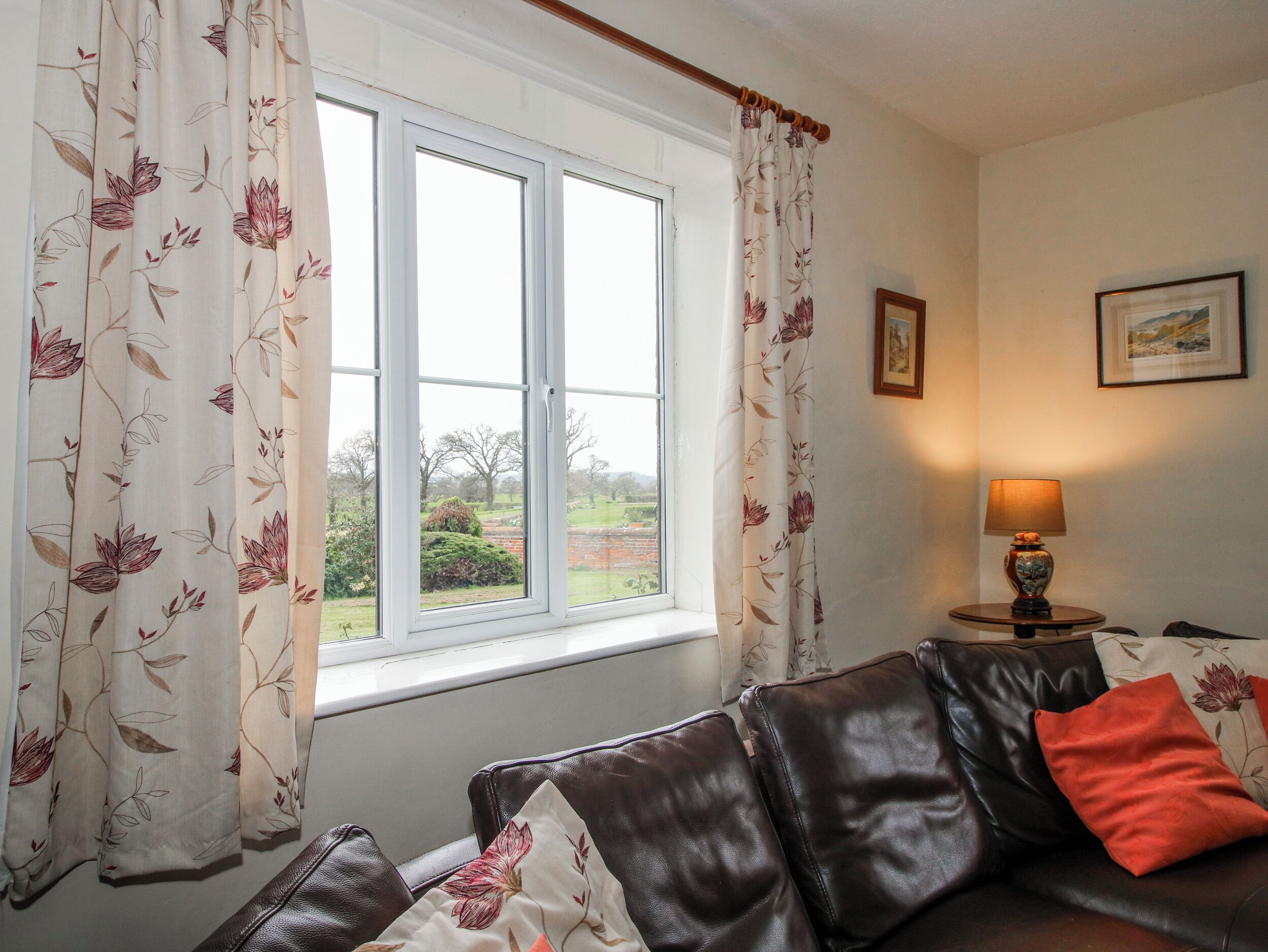 A room with a window, a leather sofa, a lamp, and a framed picture on the wall.