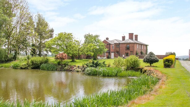 A large brick building with a pond in the foreground, surrounded by lush greenery and trees. - The Manor House at Kenwick Lodge (Ellesmere)