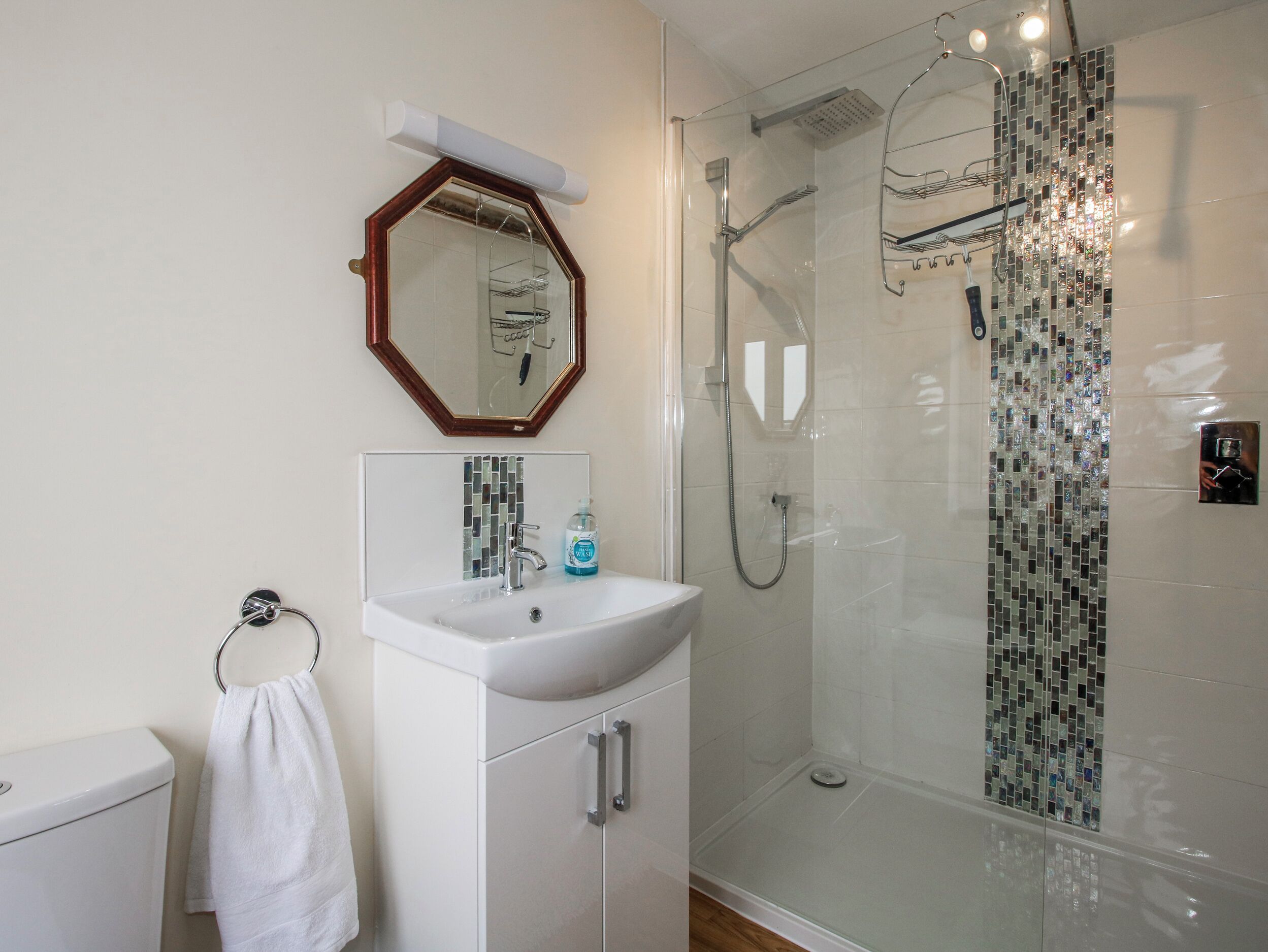 Un baño con cabina de ducha de vidrio, un lavamanos blanco con un espejo encima y un perchero para toallas.