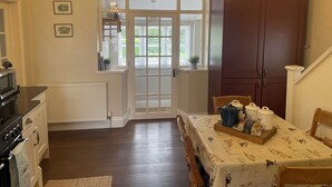 A cozy kitchen with a dining table set for four, a large wooden cabinet, and a window with a view of greenery. - Warren House Cottage (Market Rasen)