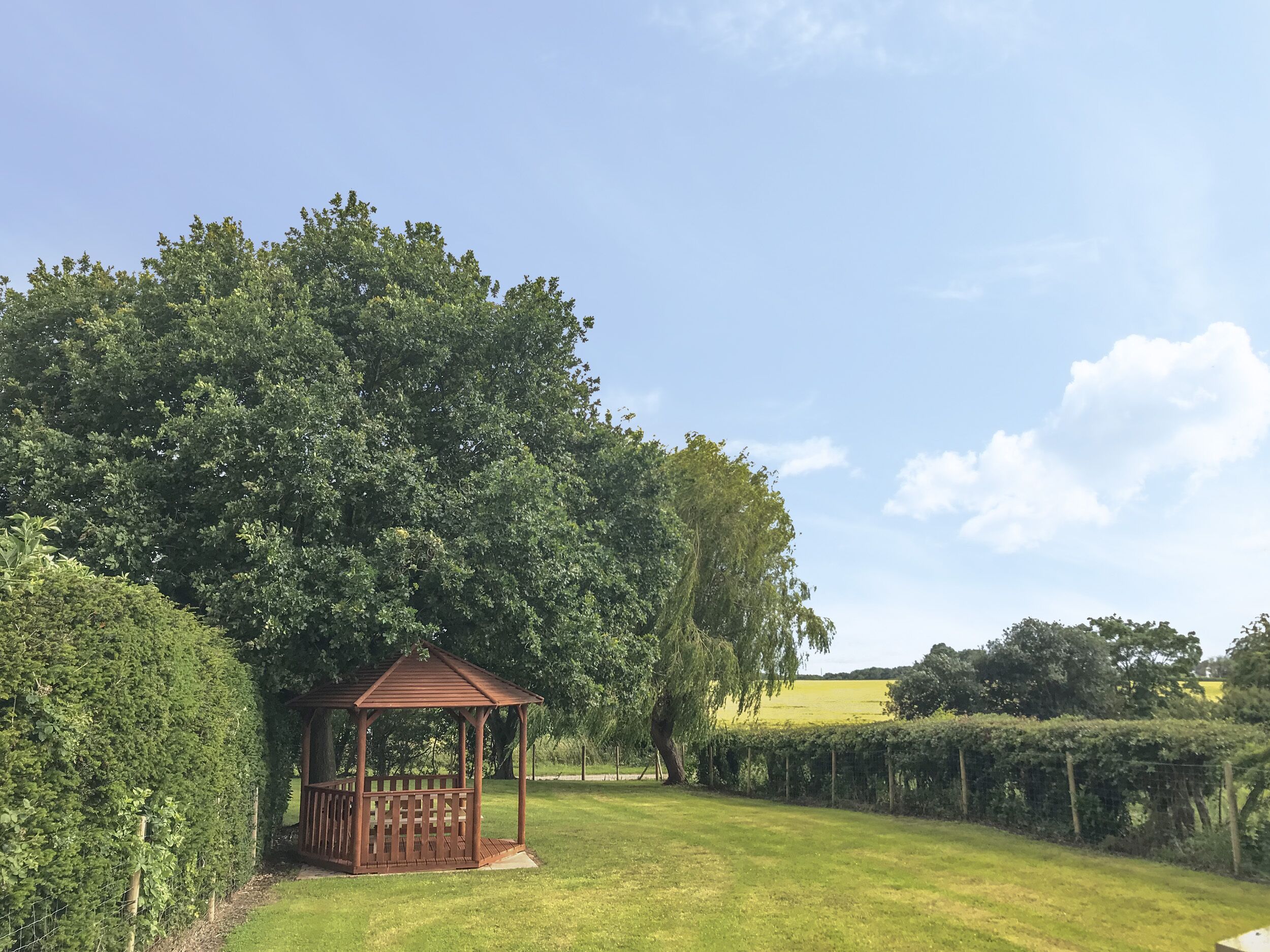 A gazebo in a grassy area with trees and a fence in the background.