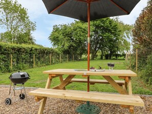 Una mesa de picnic de madera con una sombrilla, una parrilla para barbacoa y una botella de vino.
