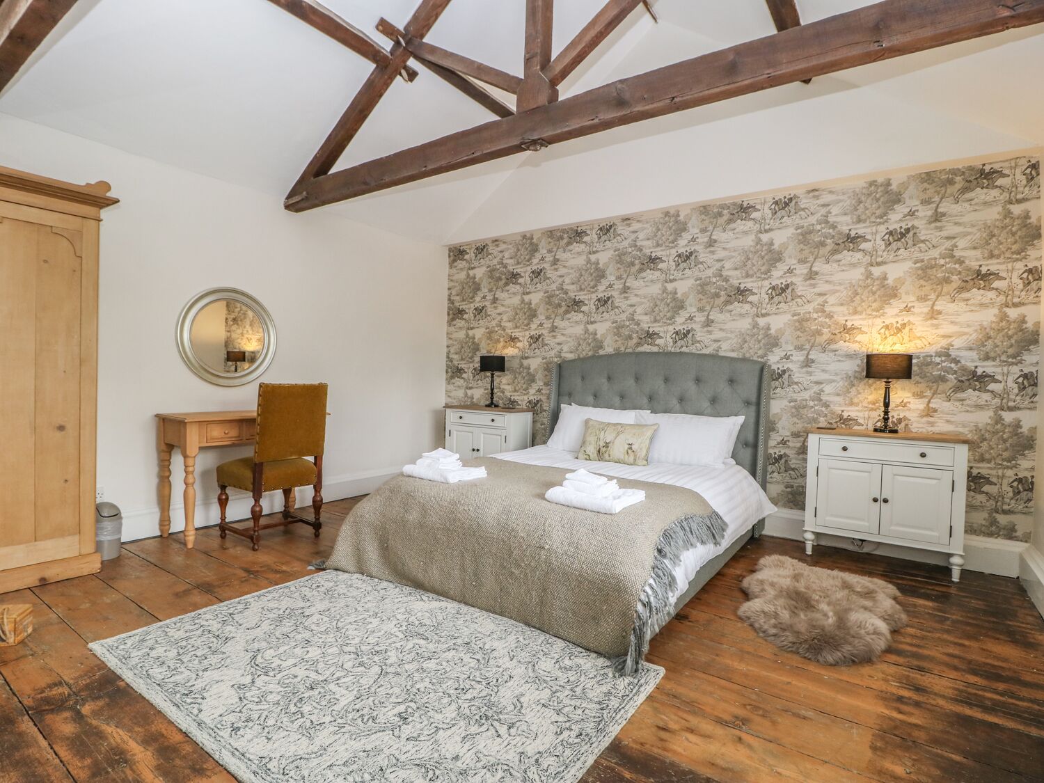 Une chambre à coucher avec un grand lit, un bureau en bois, une chaise, un miroir et une table de chevet avec une lampe.