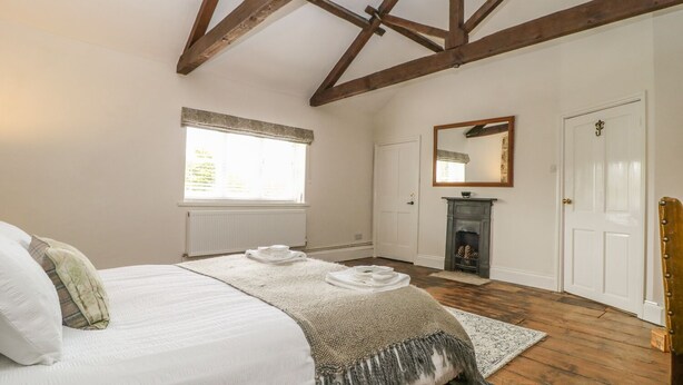 A bedroom with a large bed, a fireplace, a window with blinds, and a door. - Warren House Cottage (Market Rasen)