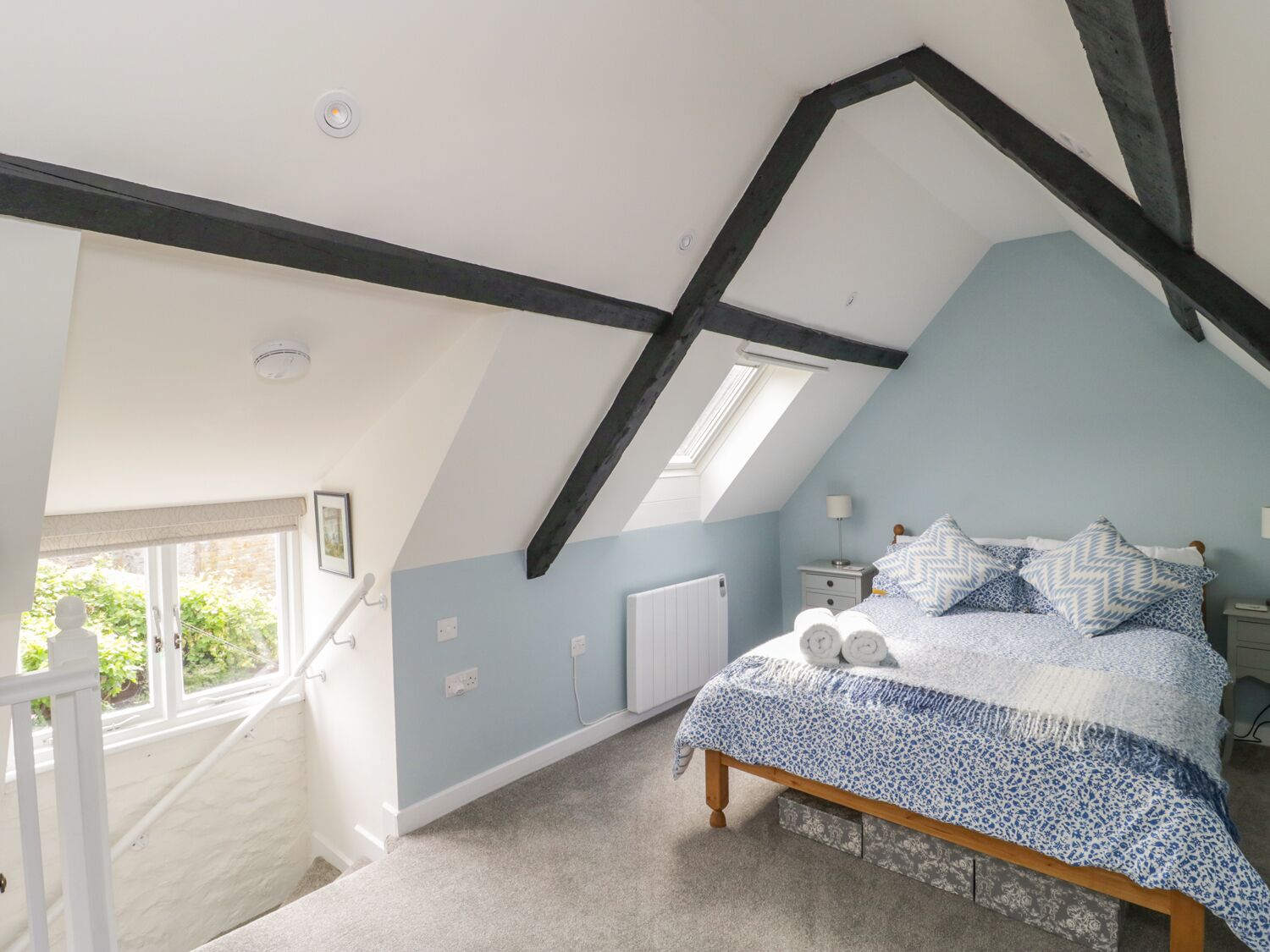 A bedroom with a sloped ceiling, a bed with patterned bedding, a nightstand, and a window with a view of greenery.