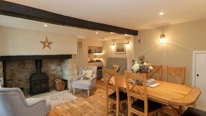 A cozy living room with a stone fireplace, a dining table with wooden chairs, and a comfortable seating area with a sofa and armchairs. - Market House (Weymouth)