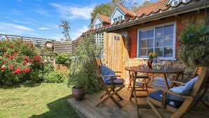 A wooden deck with outdoor furniture, a potted plant, and a window with a view of the garden. - Gables Cottage (Market Rasen)