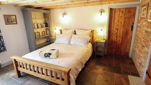 A bedroom with a wooden bed, a bookshelf, a nightstand, and a brick wall. - Gables Cottage (Market Rasen)