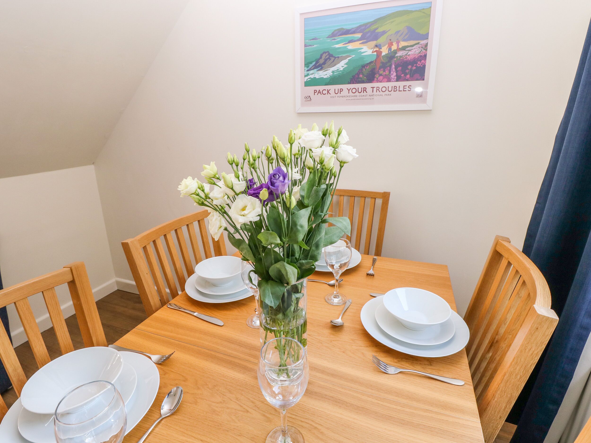 Mesa para cuatro personas, con platos blancos, cubiertos y un jarrón de flores.