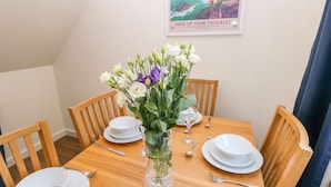 A dining table set with white plates, silverware, and a vase of white and purple flowers. - Little Freestone (Kilgetty)