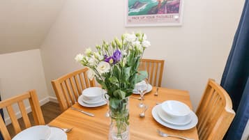 Mesa para cuatro personas, con platos blancos, cubiertos y un jarrón de flores.