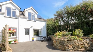 A white two-story house with a stone wall garden, a solar panel, and a clear sky. - Little Freestone (Kilgetty)