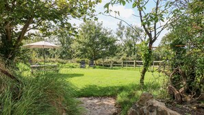 A stone pathway leading to a grassy area with a wooden fence and chairs. - Little Freestone (Kilgetty)