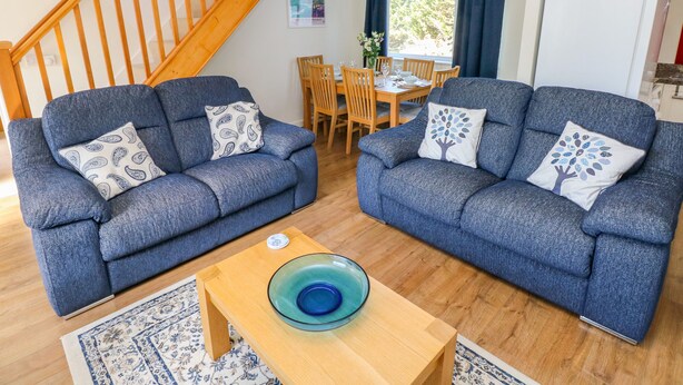 A living room with two blue sofas, a wooden coffee table, and a dining area with wooden chairs and a table. - Little Freestone (Kilgetty)