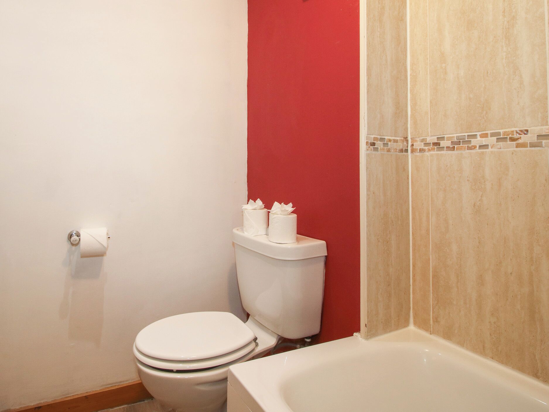 Un baño con inodoro, bañera y una pared de acento roja.