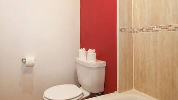 Un baño con inodoro, bañera y una pared de acento roja.