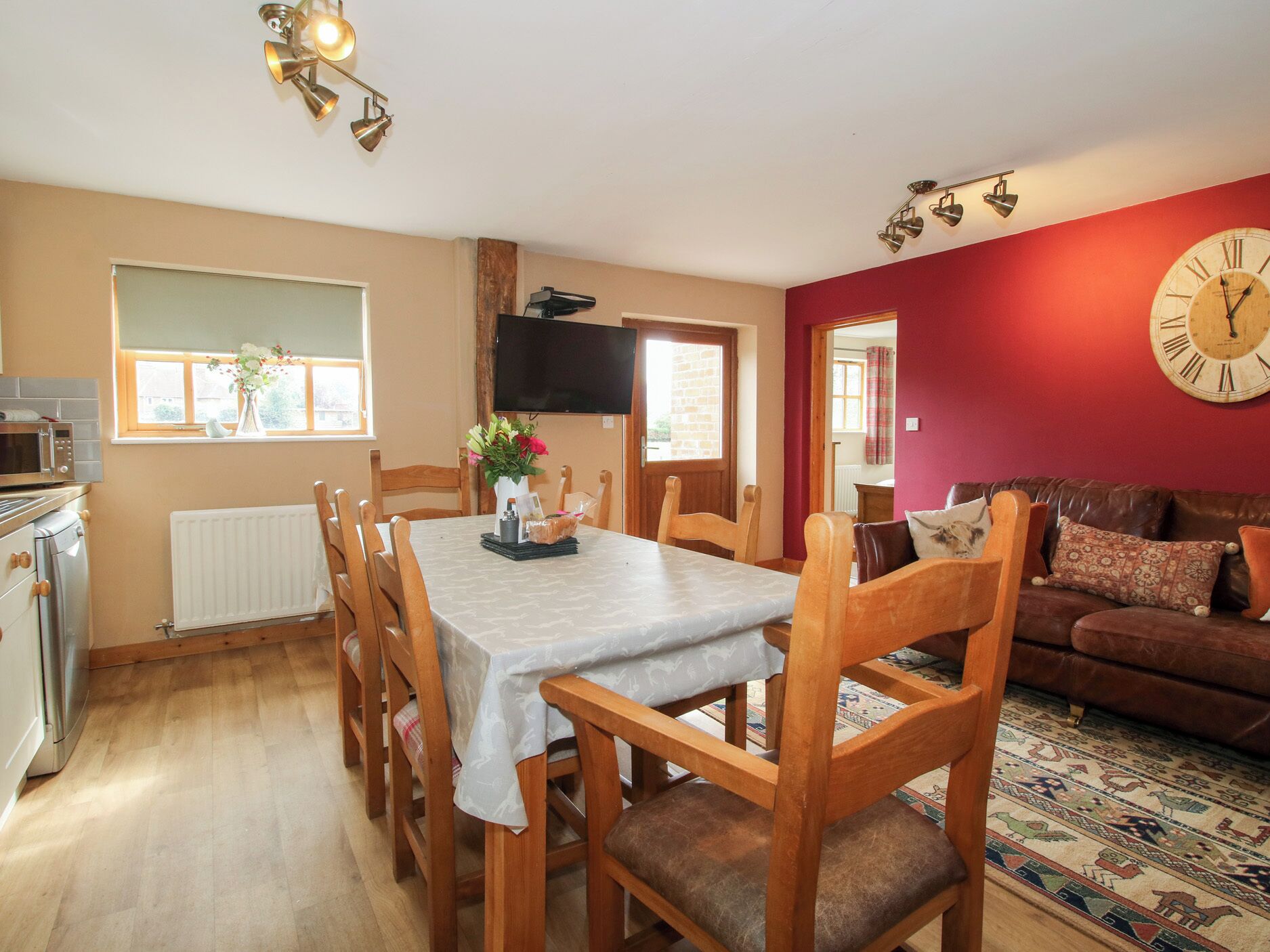 A dining area with a table set for four, wooden chairs, a vase with flowers, and a flat-screen TV mounted on the wall.