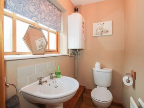 Une salle de bain avec un lavabo blanc, des toilettes et une fenêtre ornée d’un rideau à motifs floraux.
