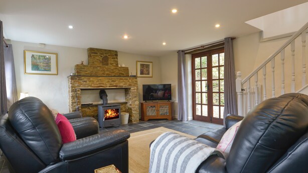 Una sala de estar con chimenea de piedra, sof ás de cuero, un televisor y una escalera.