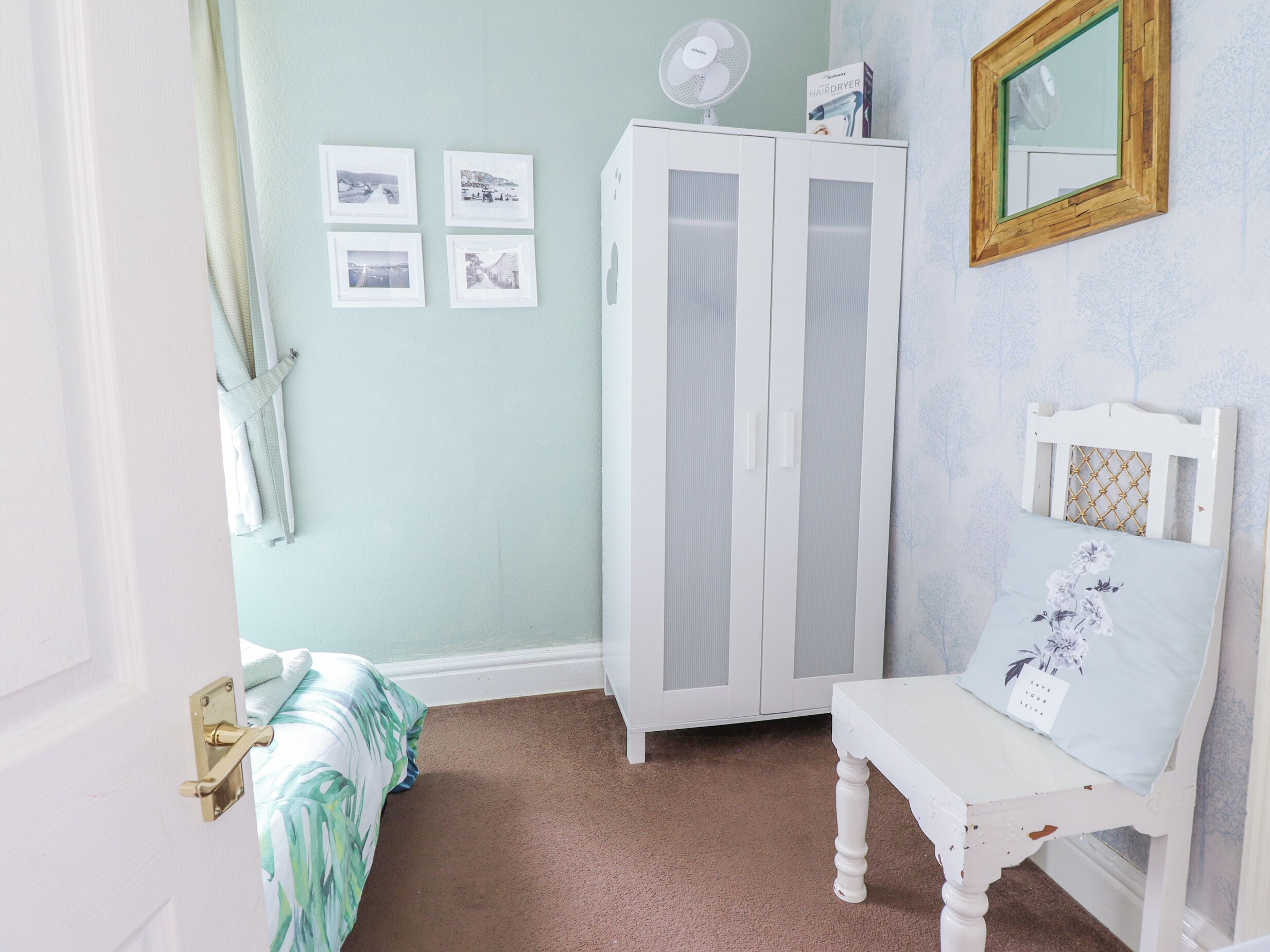 Une chambre à coucher avec un lit, une armoire blanche, un miroir et une petite table.