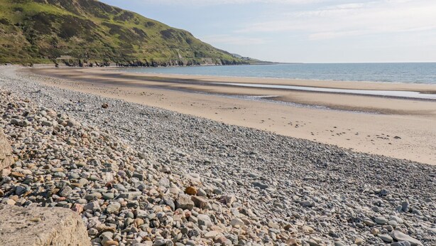 A pebbled beach with a rocky foreground and a gentle slope leading to the sea.