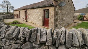 Un edificio de piedra con una puerta roja, una antena parabólica y un muro de piedra al frente.