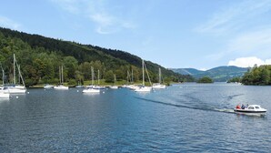 Ein See mit mehreren Segelbooten, die vor Anker liegen, umgeben von bewaldeten Hügeln.