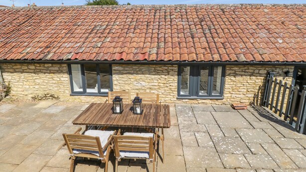 A stone building with a tiled roof, a wooden table with chairs, and a small outdoor area. - Puddleducks (Sherborne)