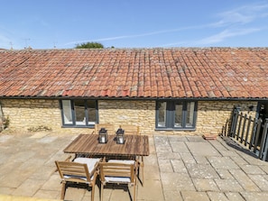 A stone building with a tiled roof, a wooden table with chairs, and a small outdoor area. - Puddleducks (Sherborne)