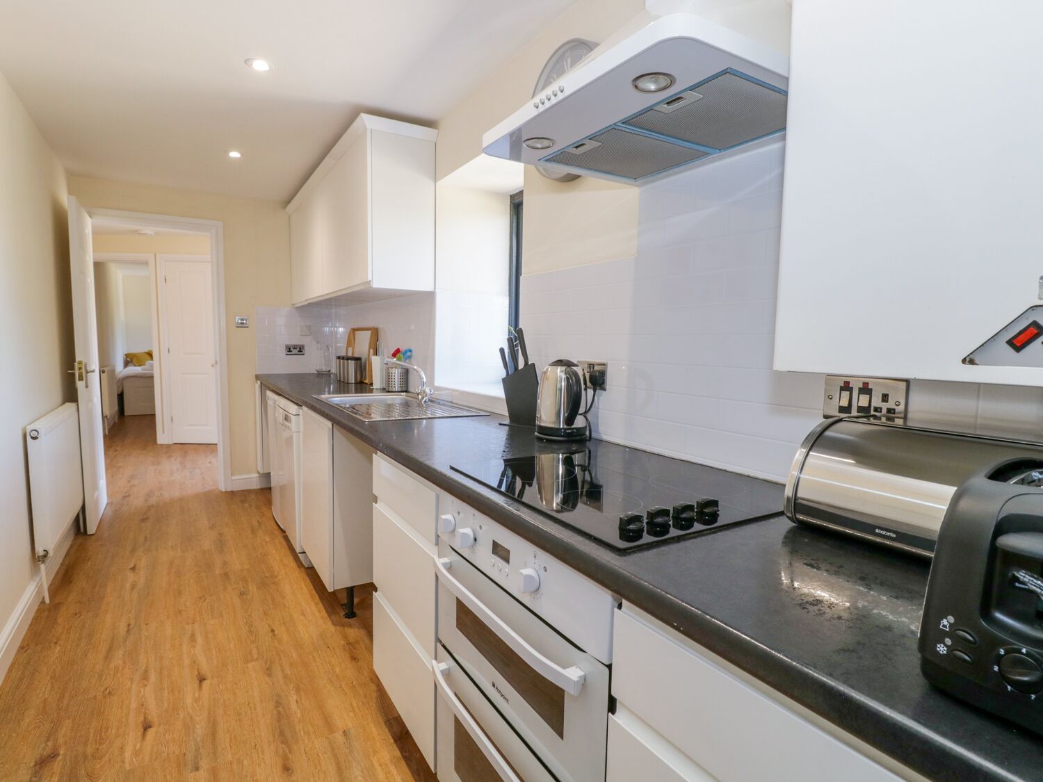 A modern kitchen with white cabinets, a black countertop, a built-in oven, and a toaster.
