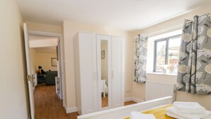A hotel room with a bed, a wardrobe, a mirror, a window with curtains, and a view of the outside. - Puddleducks (Sherborne)