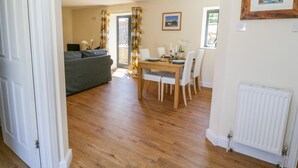 A dining area with a wooden table set for four, a grey sofa, and a window with curtains. - Puddleducks (Sherborne)