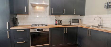 A modern kitchen with dark cabinets, a stainless steel range hood, a microwave, and a sink.