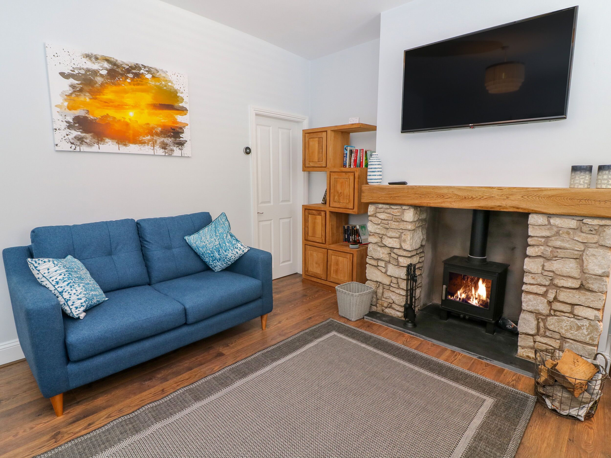 A living room with a blue sofa, a stone fireplace, a television mounted on the wall, and a bookshelf.