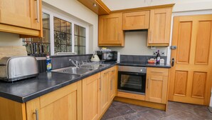 Une cuisine moderne avec des meubles en bois, un plan de travail noir, un four encastré et une fenêtre donnant sur la verdure.