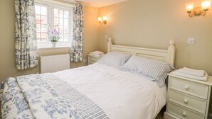Une chambre à coucher comprenant un lit, des tables de chevet, une fenêtre avec des rideaux et des luminaires fixés au mur.